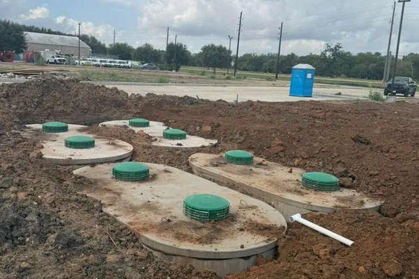 Multiple septic tanks with green lids installed on a graded commercial site
